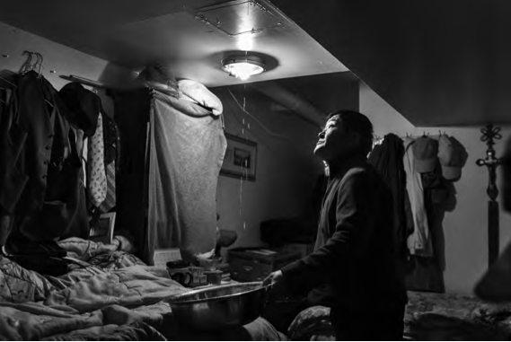 A resident at the Love Mission House collects water dropping from a leaky ceiling in the bedroom he shares with four other homeless lodgers. Photo by Yeong-Ung Yang.